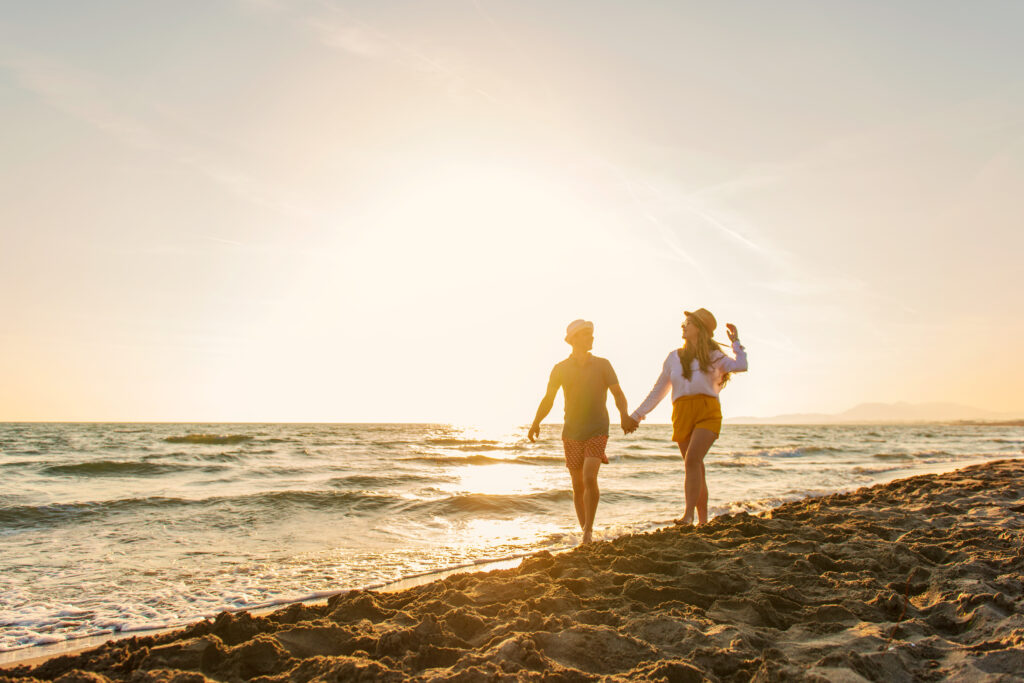 couple holding hands walking on beach at sunset